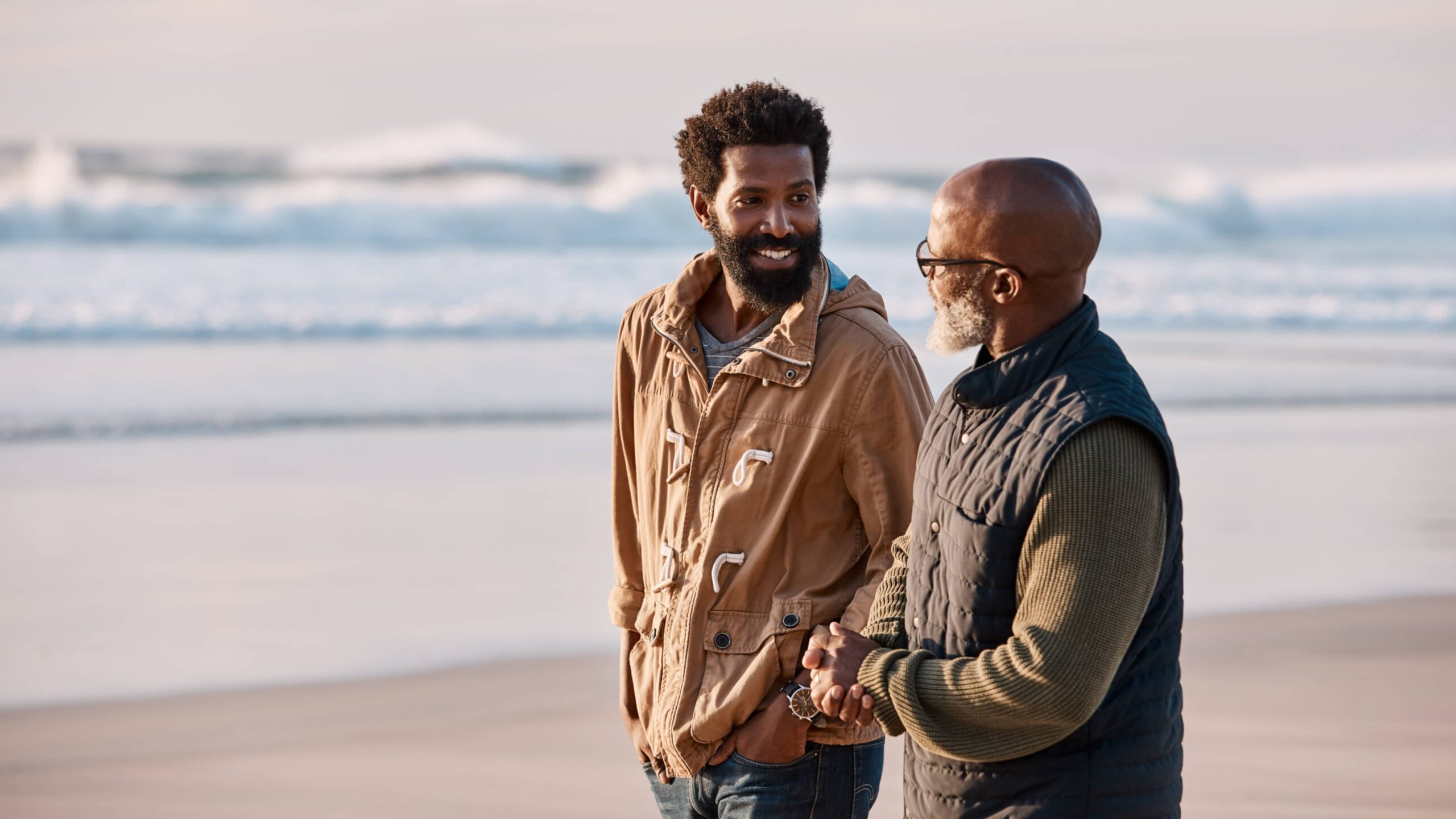 older African-American man walking on beach having a talk with his adult son